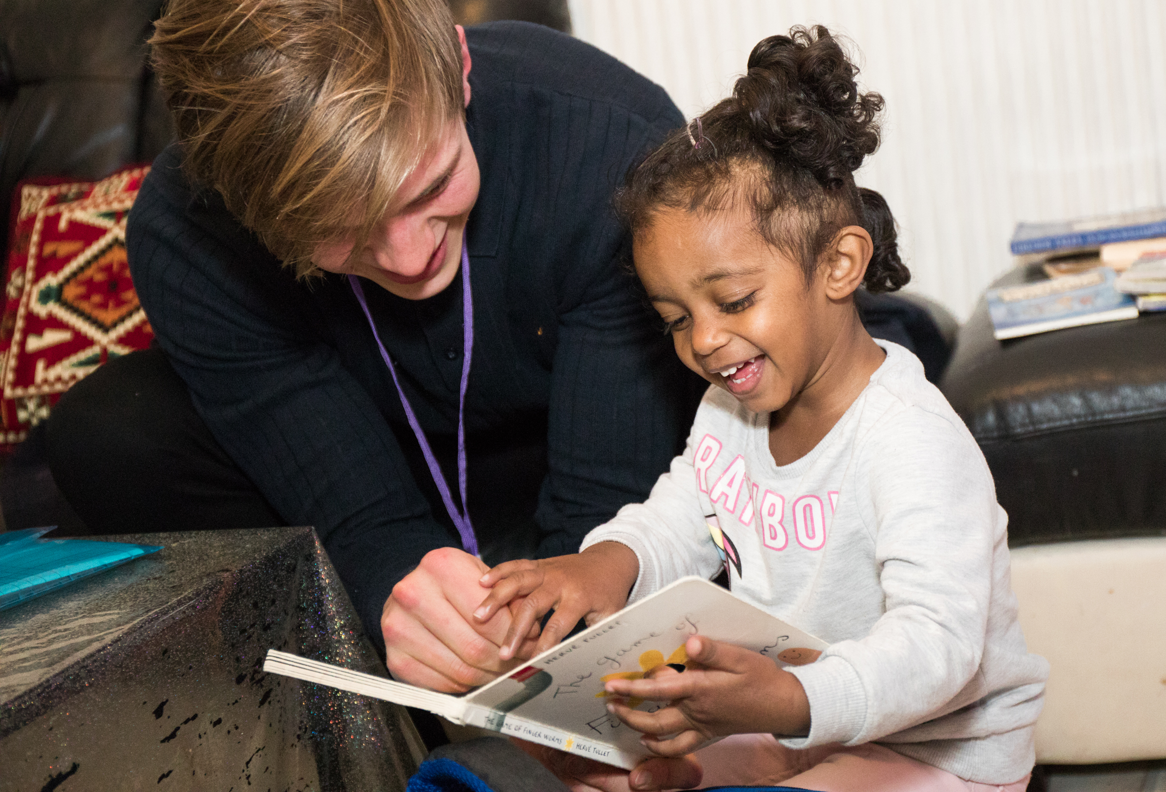 A young black child reading with the help of an adult
