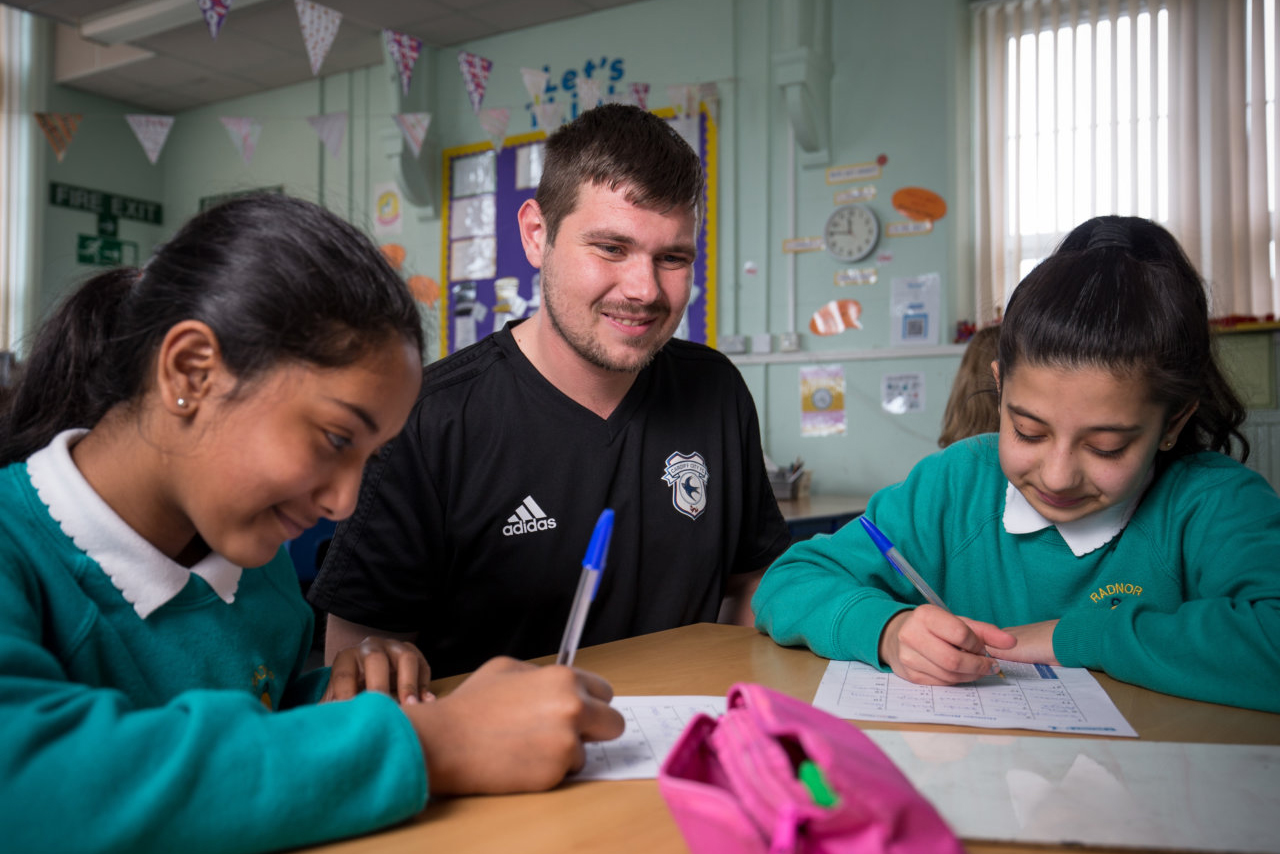 A footballer helping two children with their home work