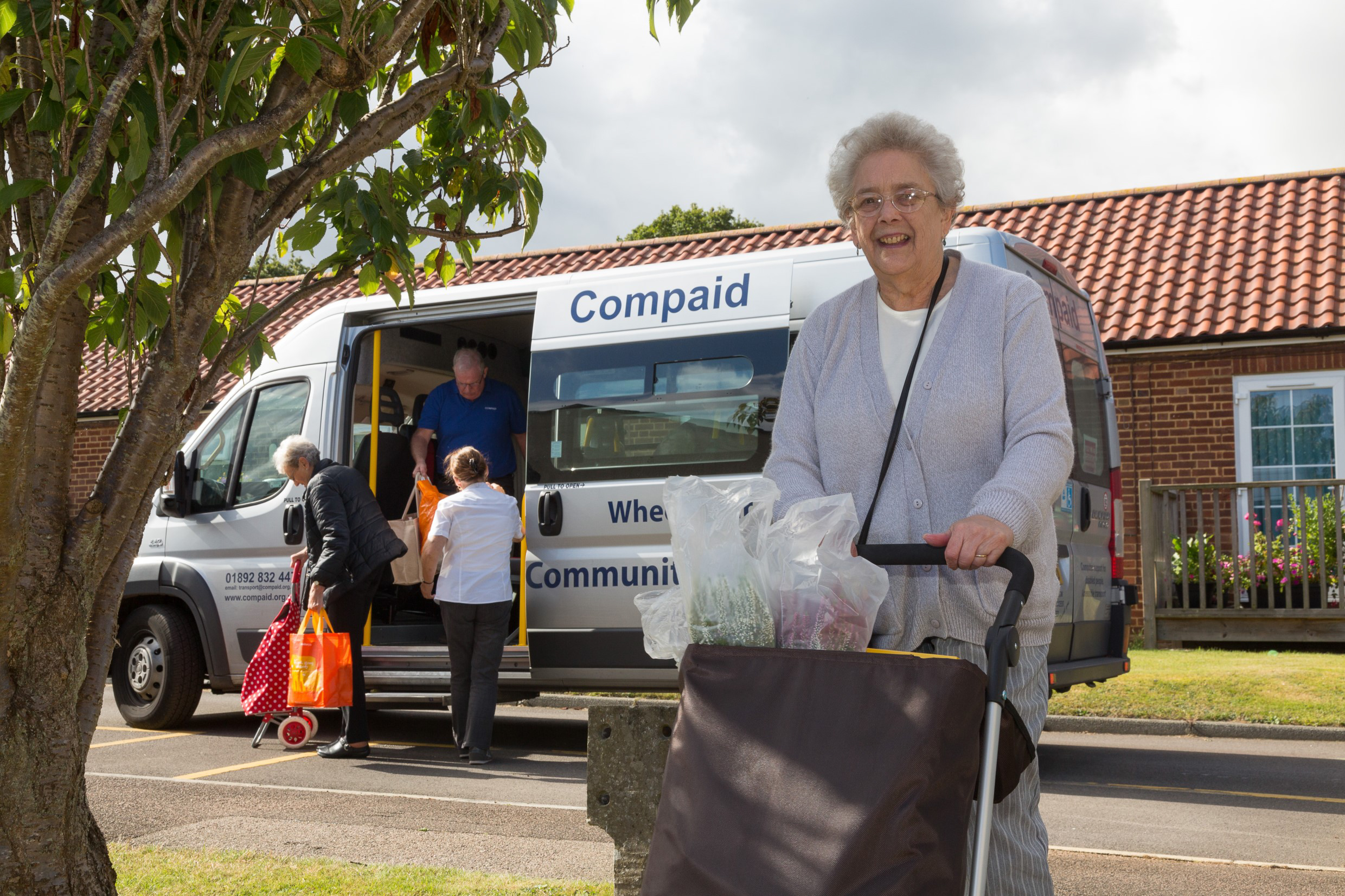 Elderly lady with a trolley standing near a Compaid mini bus