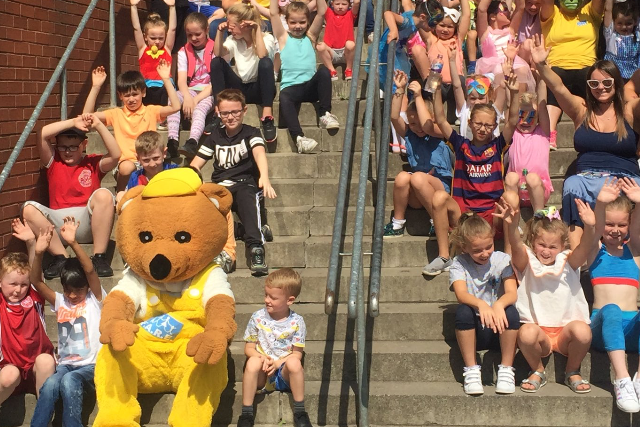 A lot of children with a bear mascot sitting on steps