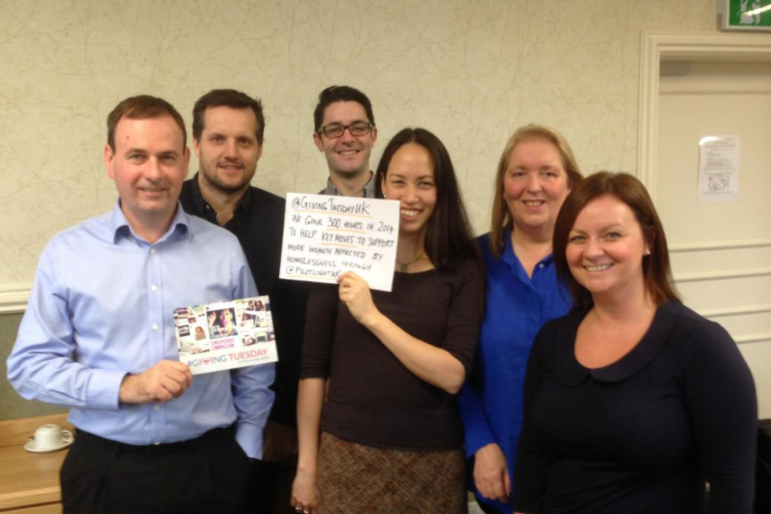 A group of people in a room with two of the people holding Giving Tuesday placards