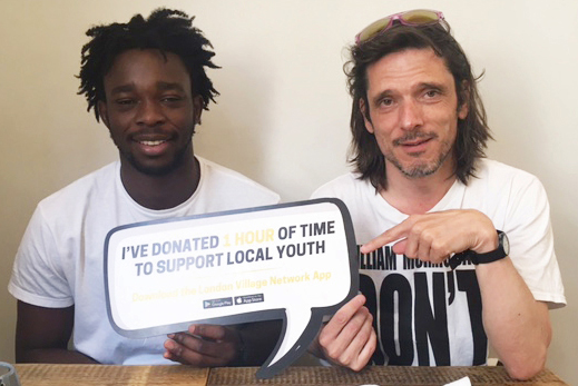 A black and a white man sitting at a table looking at a camera holding up a sign saying 'I've donated one hour of time to support local youth'.