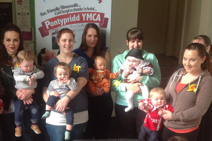 A group of mothers and babies in front of a charity banner