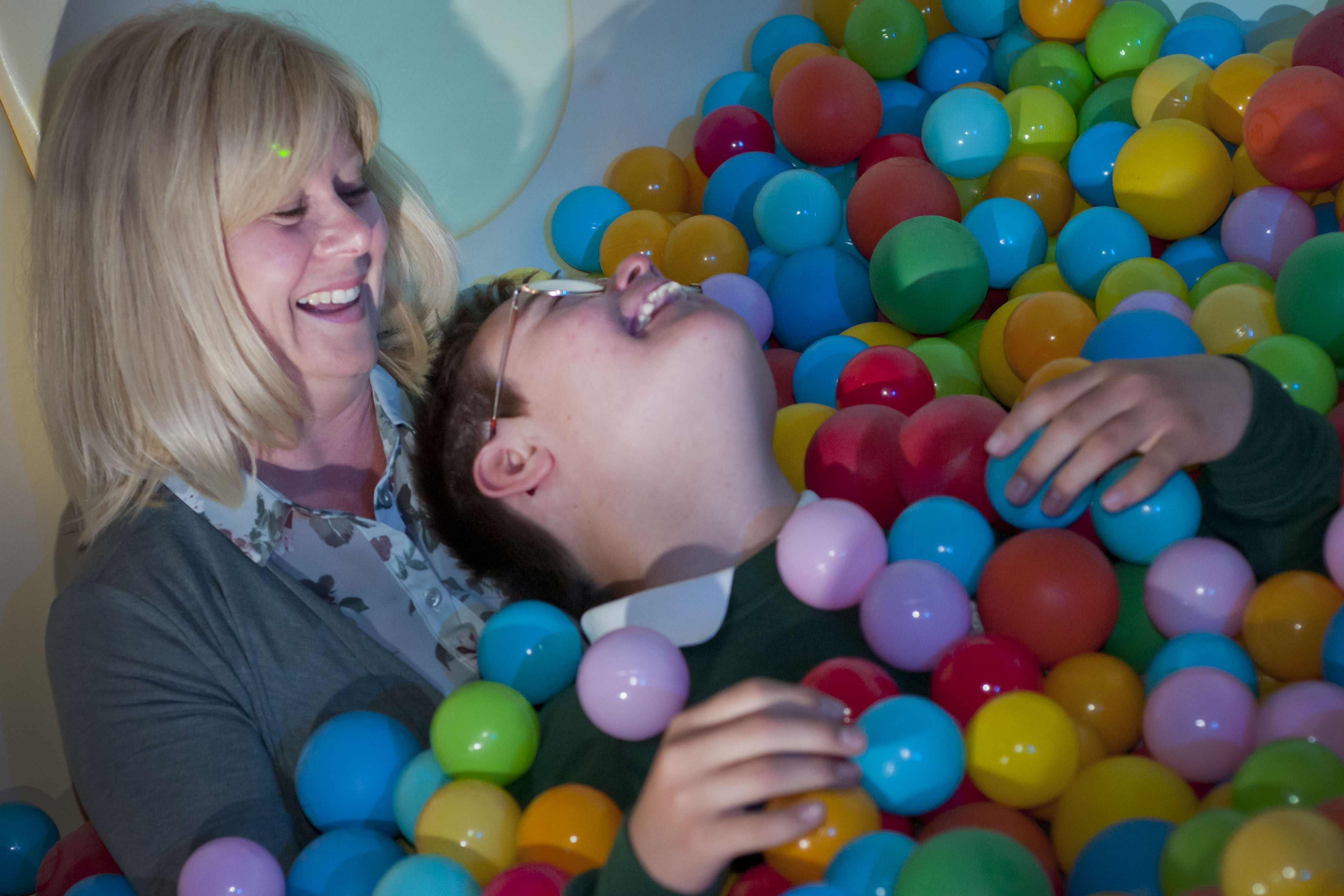 A mother holding her disabled son in a ball pit