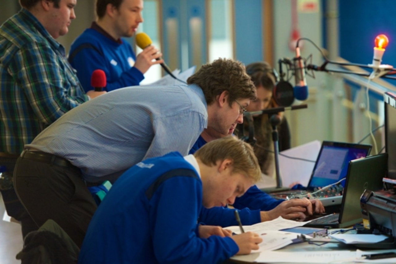 Children and adults looking at a laptop and a microphone