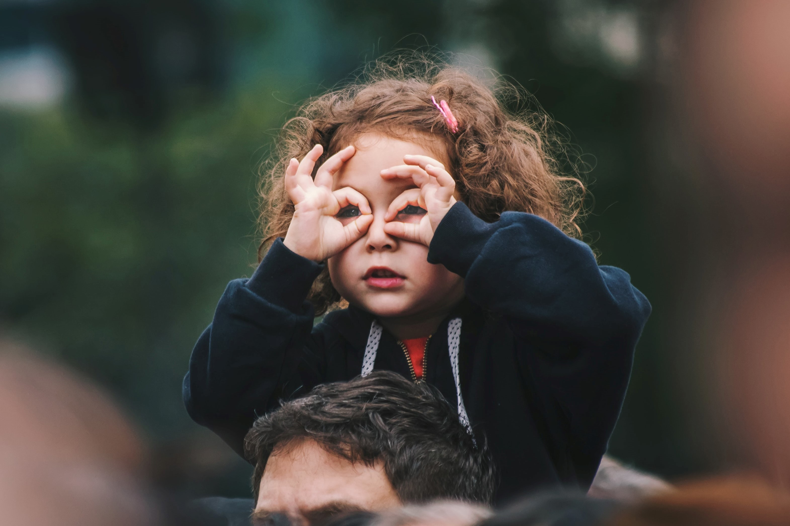 A child on her dad's shoulder with her fingers over her eyes