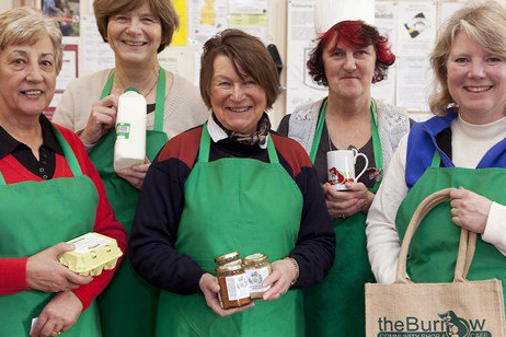 A group of women wearing green aprons and holding produce