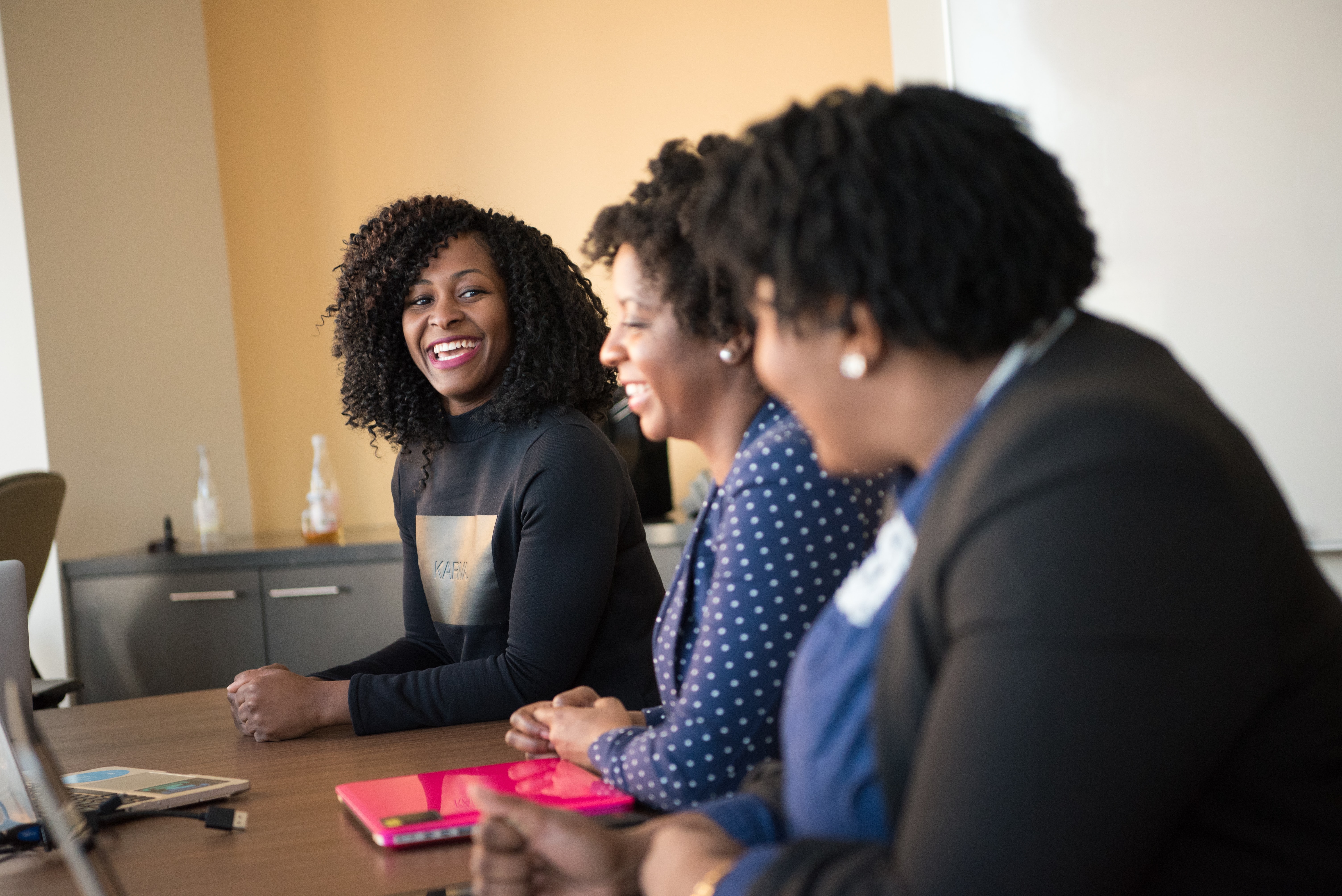 Three black women sitting in a row with one looking at the camera