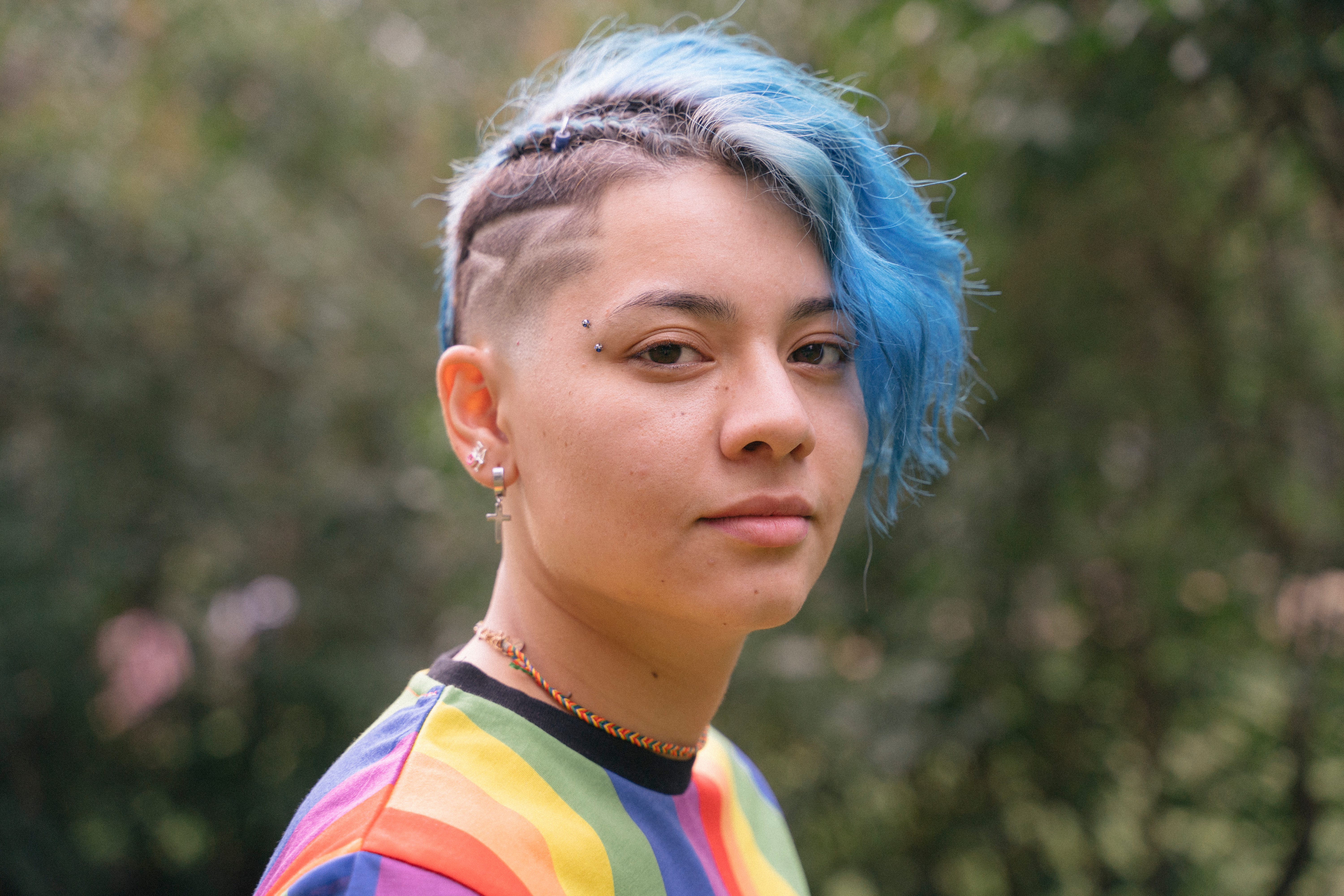 A young person with blue hair and a rainbow t shirt