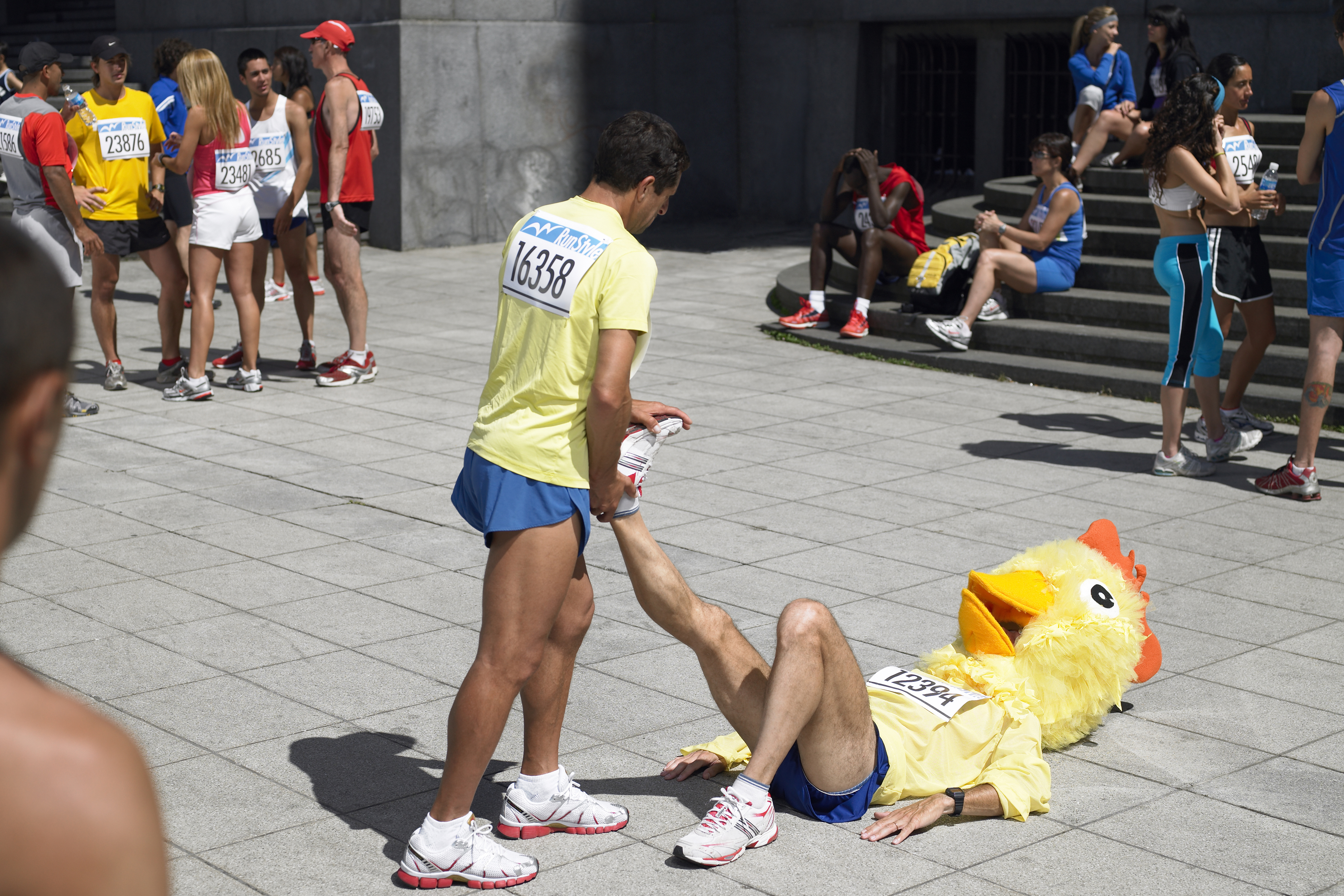 A charity runner in a chicken mask being given a foot rub by another charity runner
