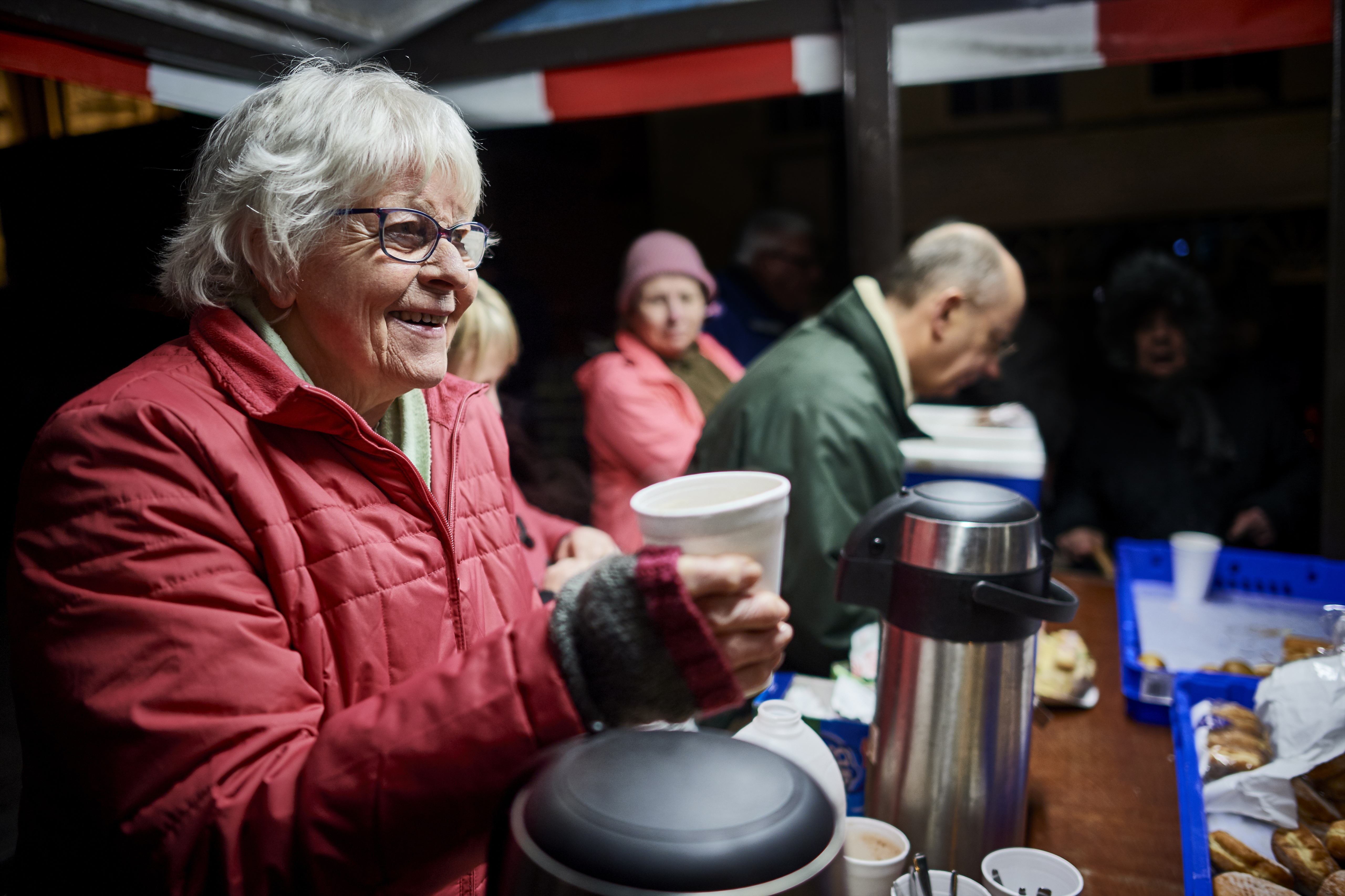 A white haired woman handing out cups of tea
