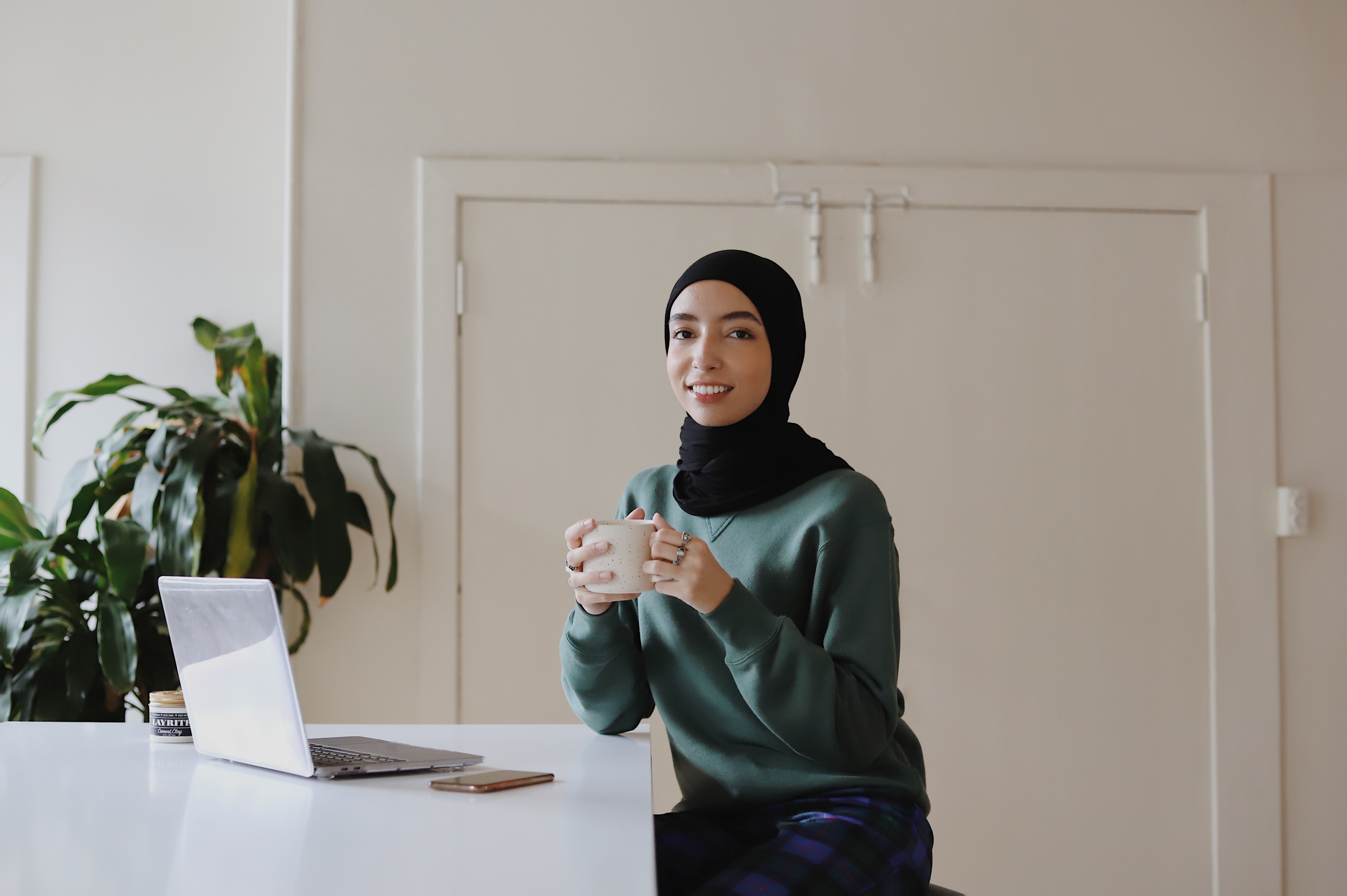 Woman wearing hijab sitting at table holding a cup