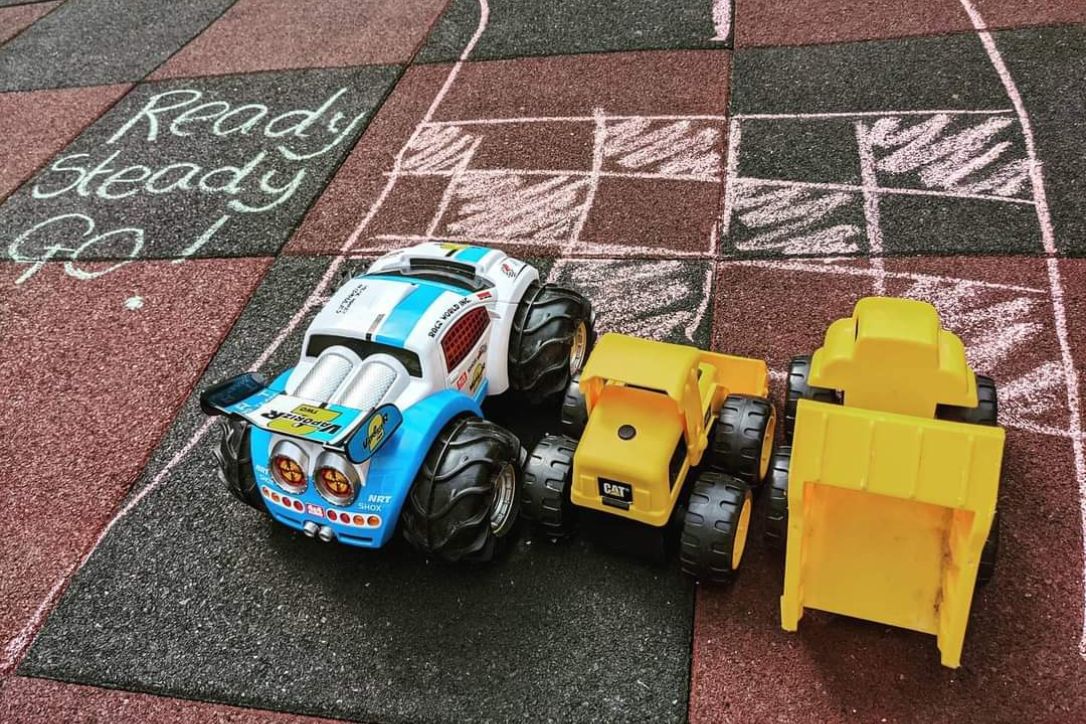 Toy cars on floor with a race track drawn in chalk and the words ready steady go!