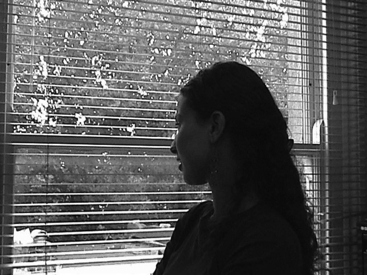 A woman standing at a window looking out of a blind